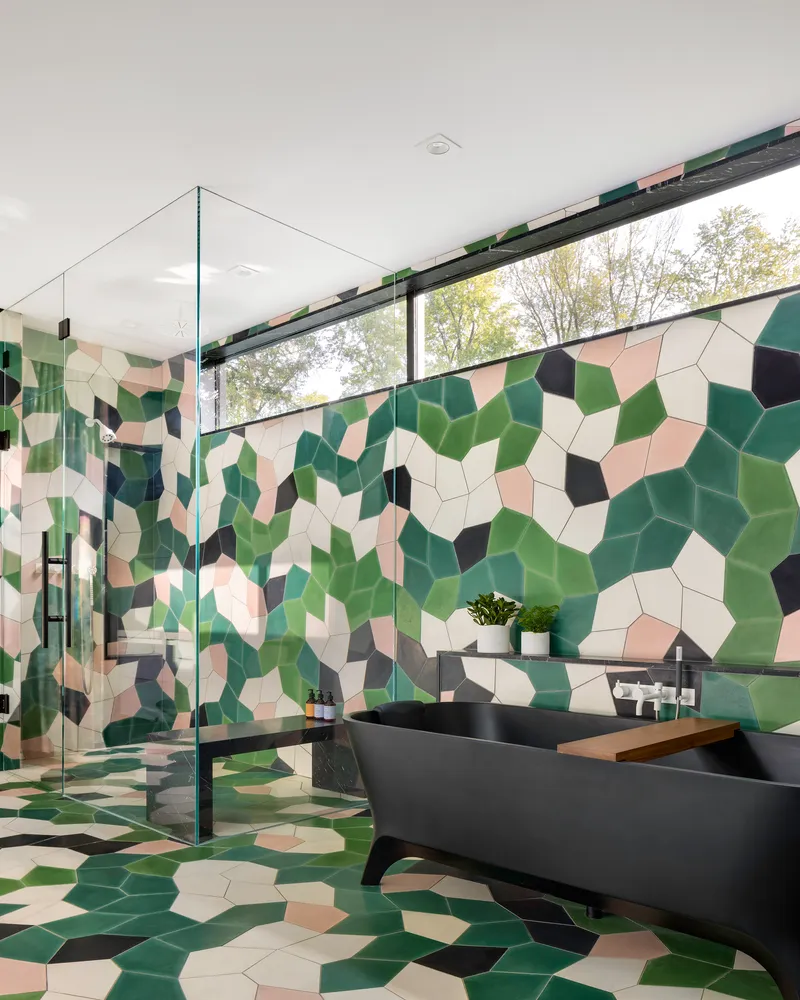 Bathroom with camouflage-patterned mosaic tile walls and floor, glass shower enclosure, and clerestory window overlooking trees
