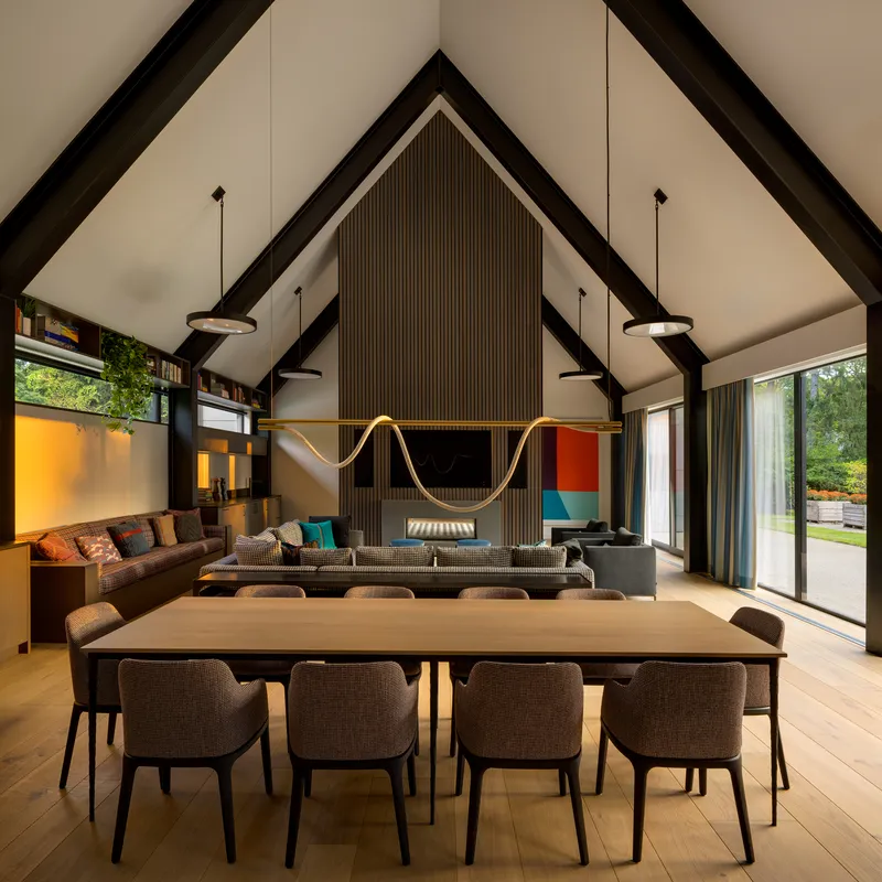 Dining table in front of vertical timber slat wall with embedded fireplace and television at dusk