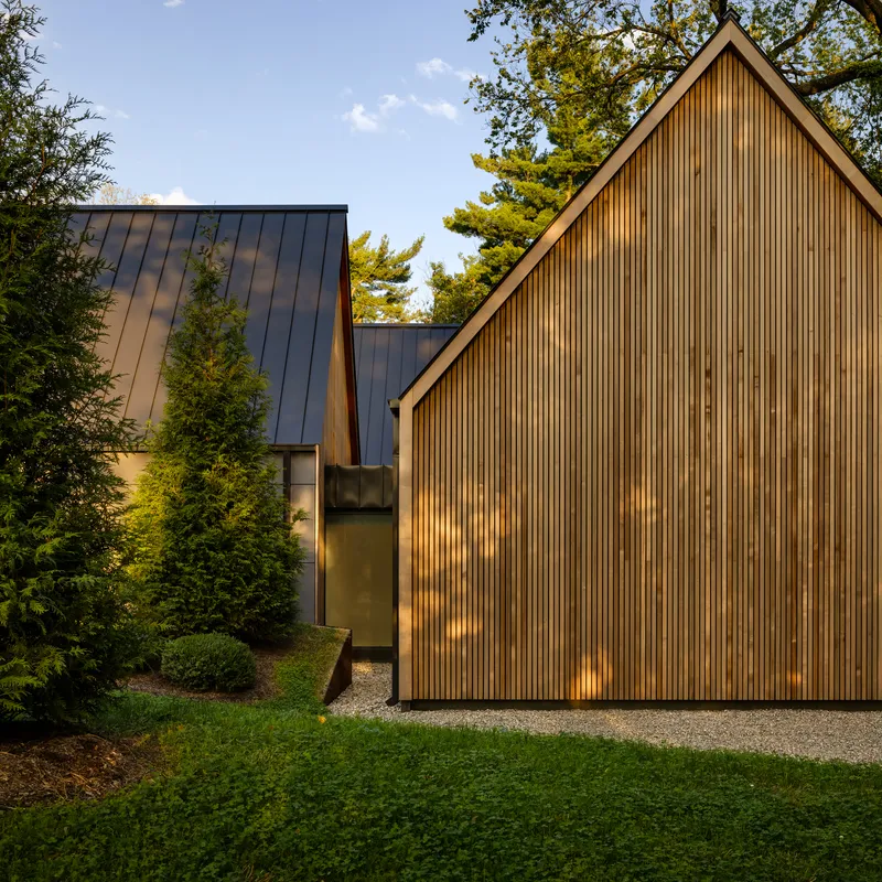 Cluster of gabled volumes in timber and metal cladding with gravel driveway at dusk