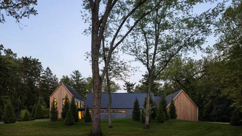 Long facade with illuminated windows flanked by timber-clad gabled volumes under a cloudy sky
