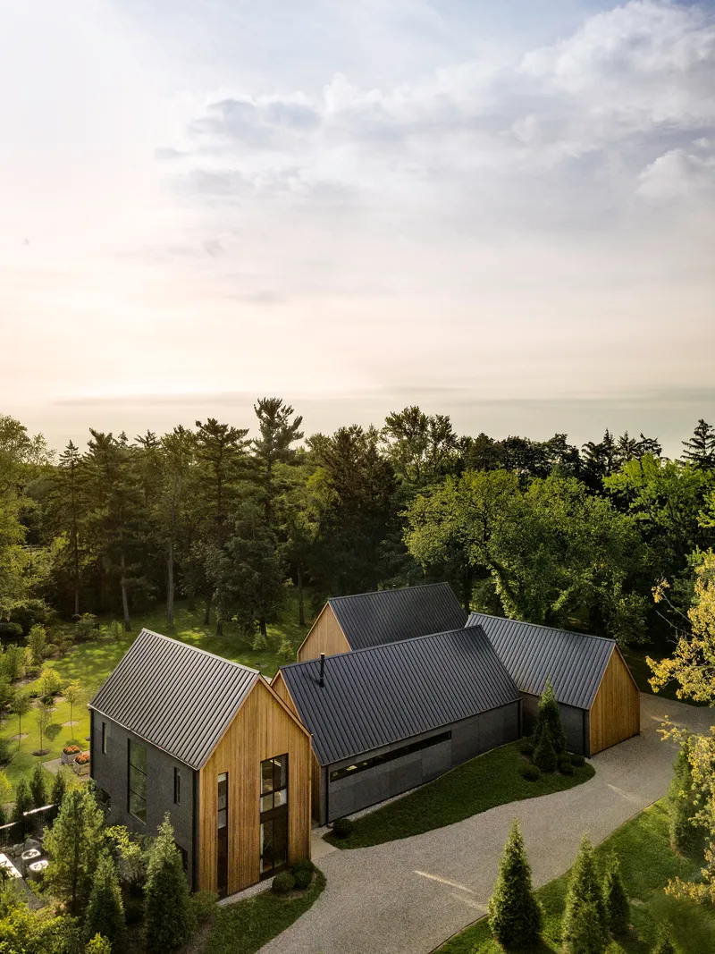Aerial view of clustered gabled volumes with metal roofs set against a forested hillside