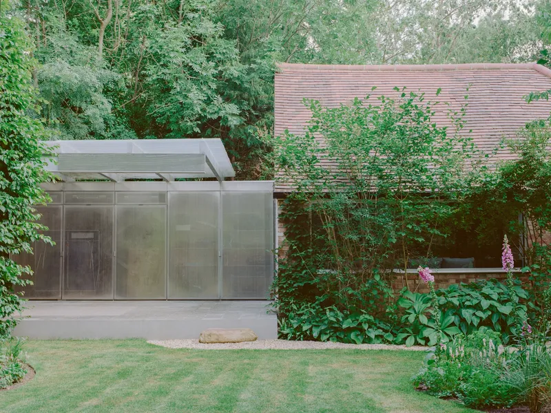 Translucent metal pavilion with flat overhang beside a horizontal timber slatted wall surrounded by garden planting