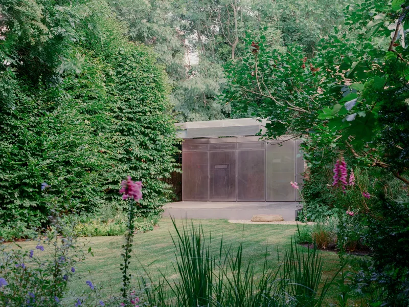 Garden view of the metal-clad pavilion volume framed by foxgloves and ornamental grasses