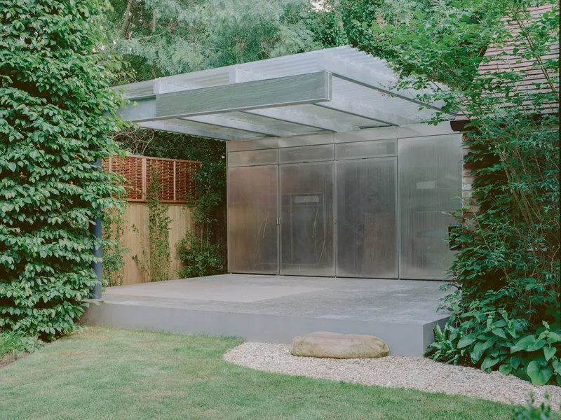 Concrete porch with gravel path leading to the translucent metal entry pavilion under a cantilevered roof
