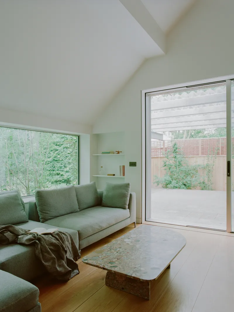 Living room with vaulted ceiling and sliding glass doors opening to the concrete terrace and garden