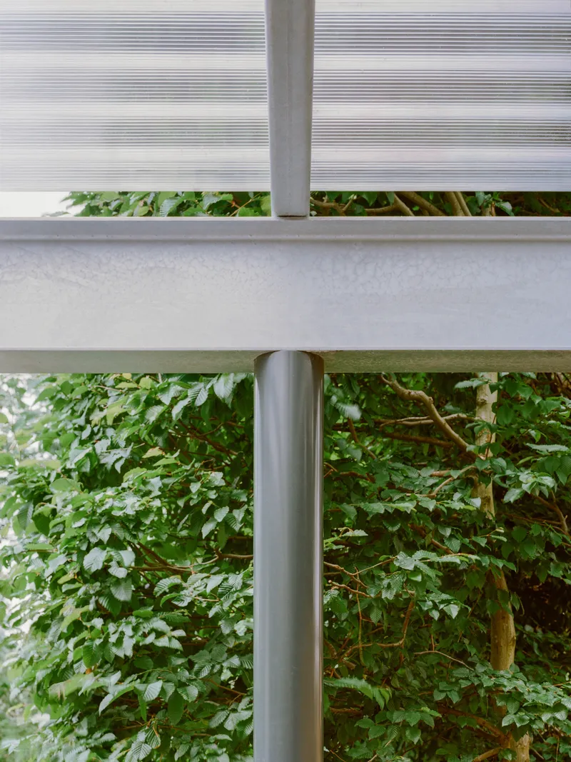 Detail of the ribbed polycarbonate canopy panel meeting a concrete beam and steel column above foliage