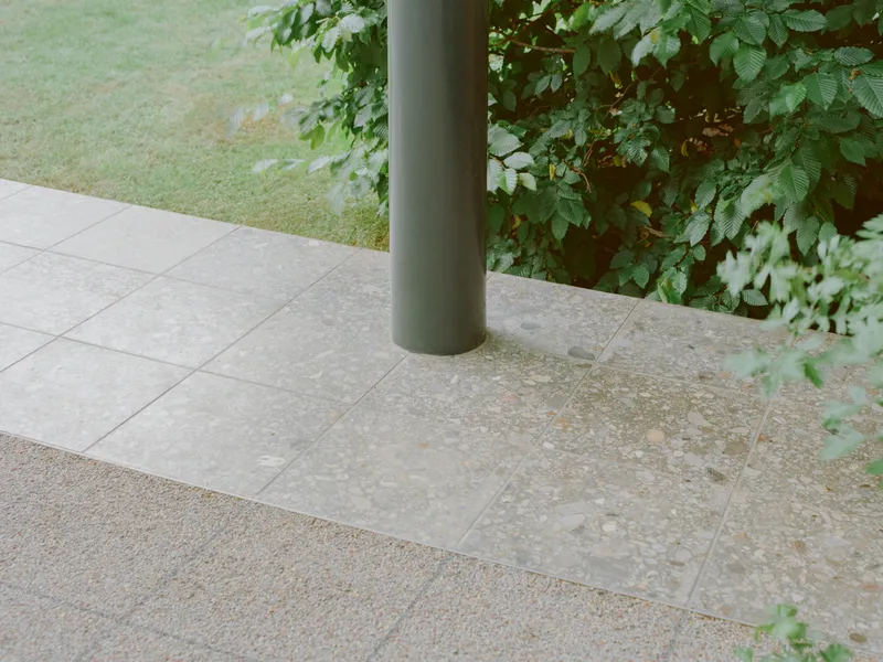 Paved terrace with large format stone tiles, cylindrical column, and gravel edge bordering the lawn