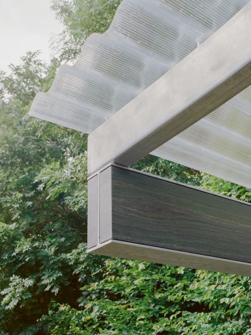 Close-up of the cantilevered beam corner showing the ribbed canopy soffit and dark timber fascia