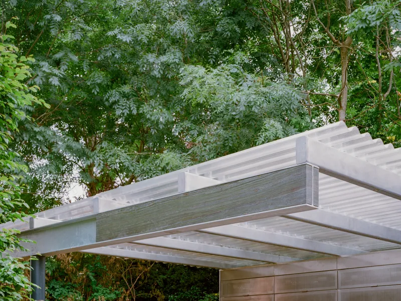 Canopy structure with exposed timber beams and translucent ribbed panels framed by surrounding trees