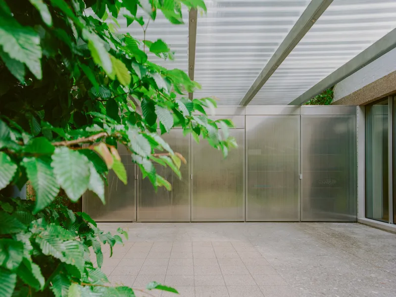 Covered entry terrace with stainless steel cabinet wall and overhanging branch filtering the light