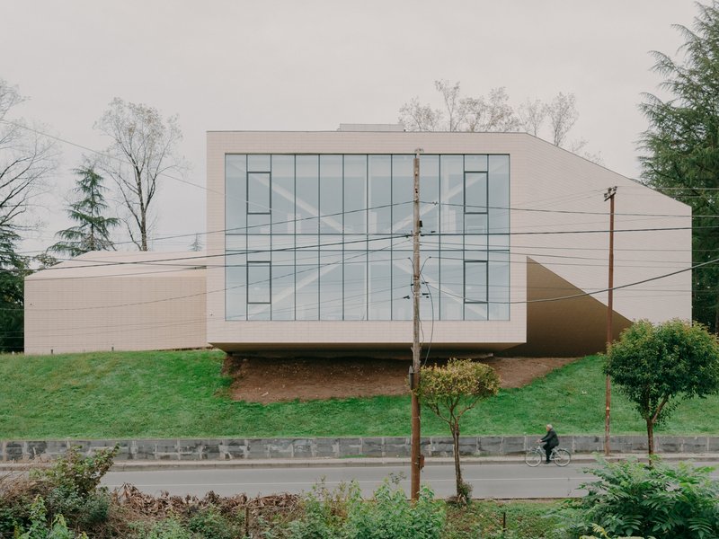 Head-on view of the glazed facade with overhead power lines and a cyclist passing on the road