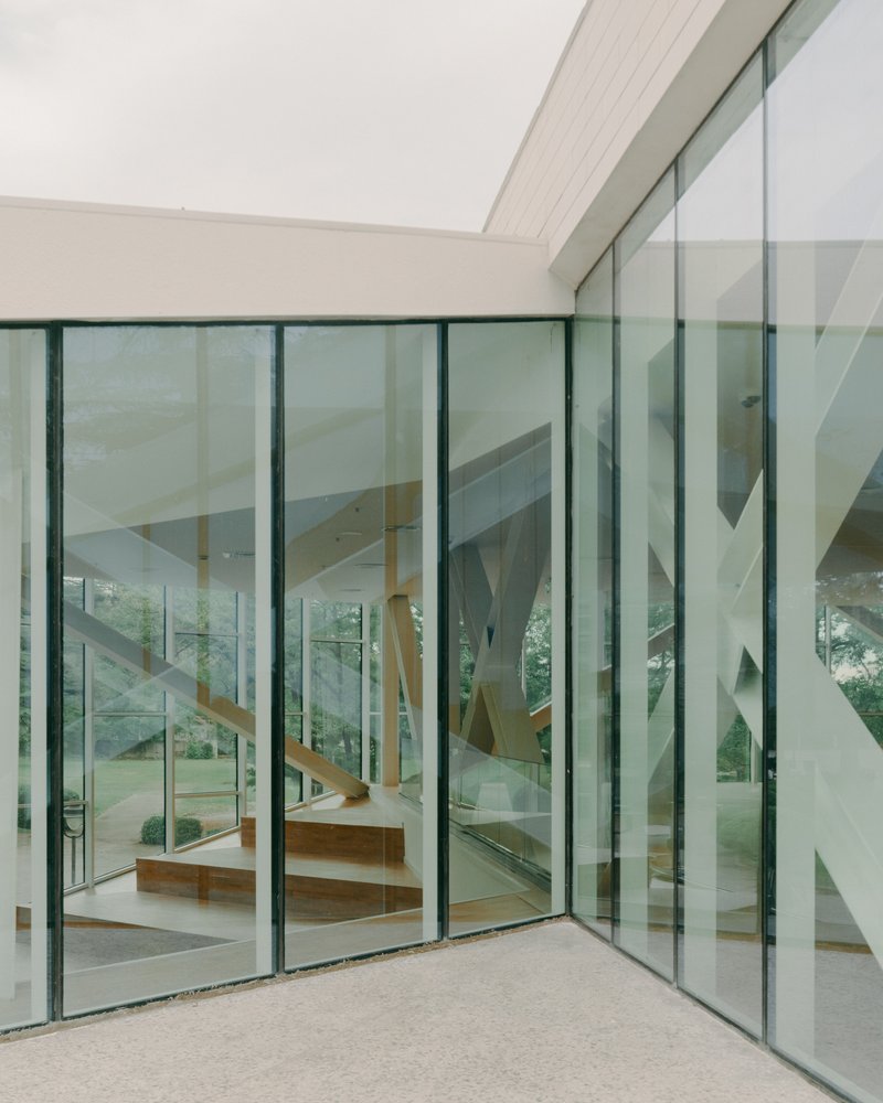 Corner courtyard enclosed by floor-to-ceiling glass walls revealing the timber staircase within