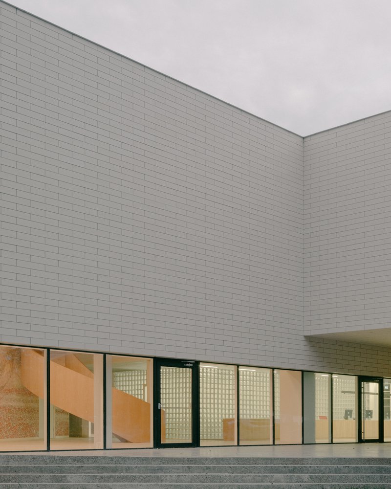 White brick facade with ribbon windows illuminated at dusk above a stepped concrete terrace