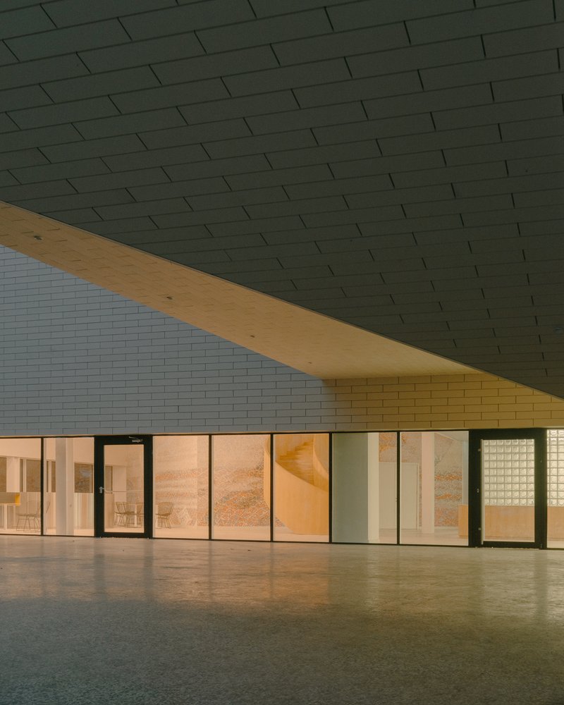 Covered entrance with green tiled soffit and timber beam spanning across glazed interior at dusk