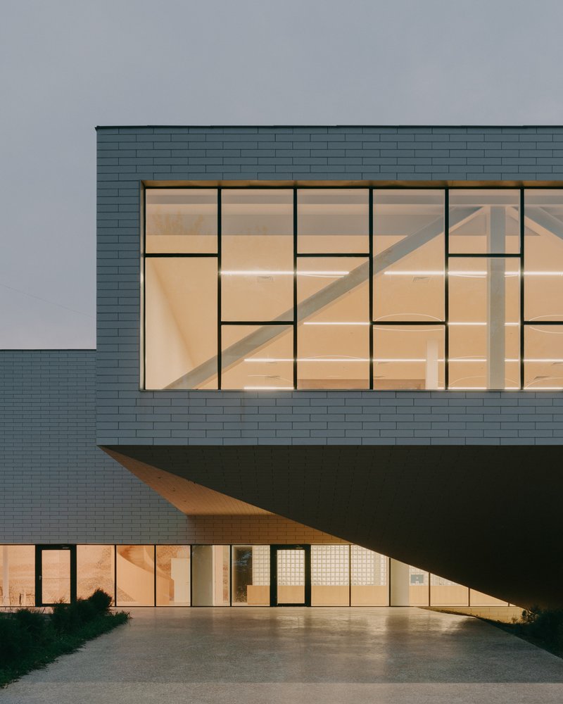 Cantilevered upper level with grid-patterned glazing illuminated at twilight above ground floor entrance
