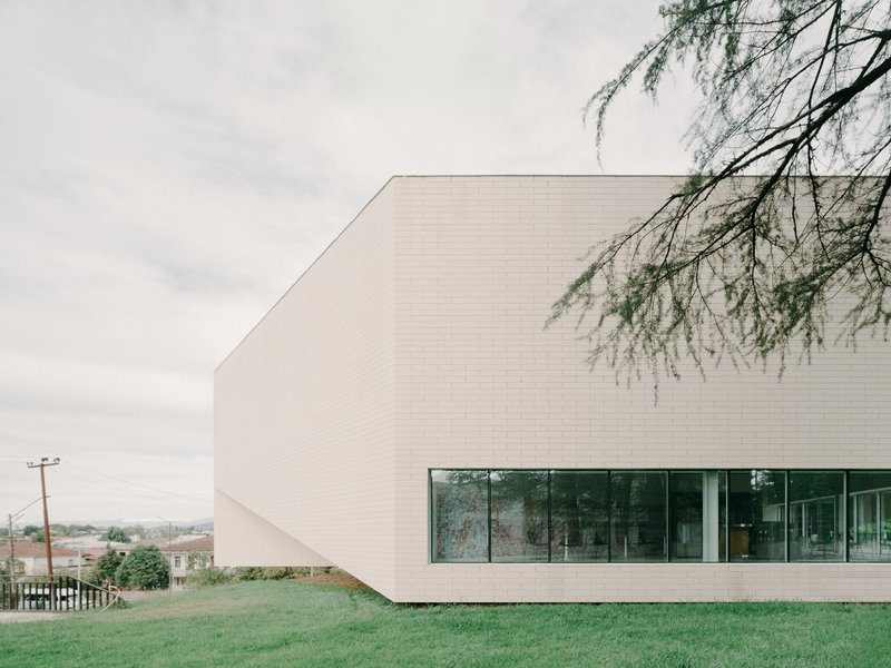 Horizontal white brick facade with ribbon window overlooking a grass lawn under overcast skies