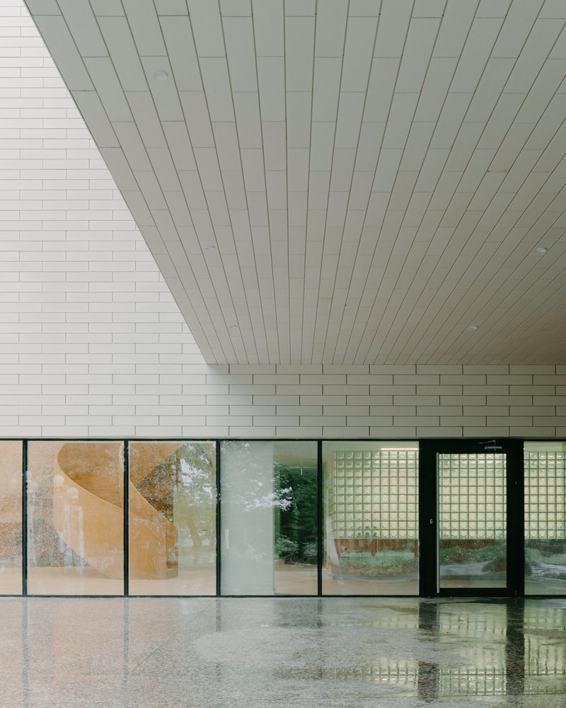 Interior lobby with polished floor and white brick wall beneath a slatted ceiling beside gridded glass doors