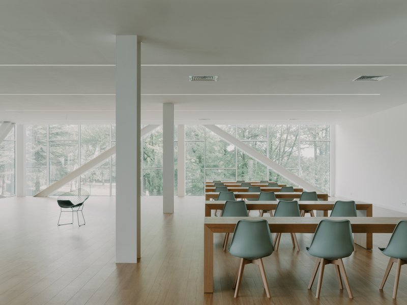 Dining hall with rows of timber tables and pale green chairs beneath white structural cross-braces