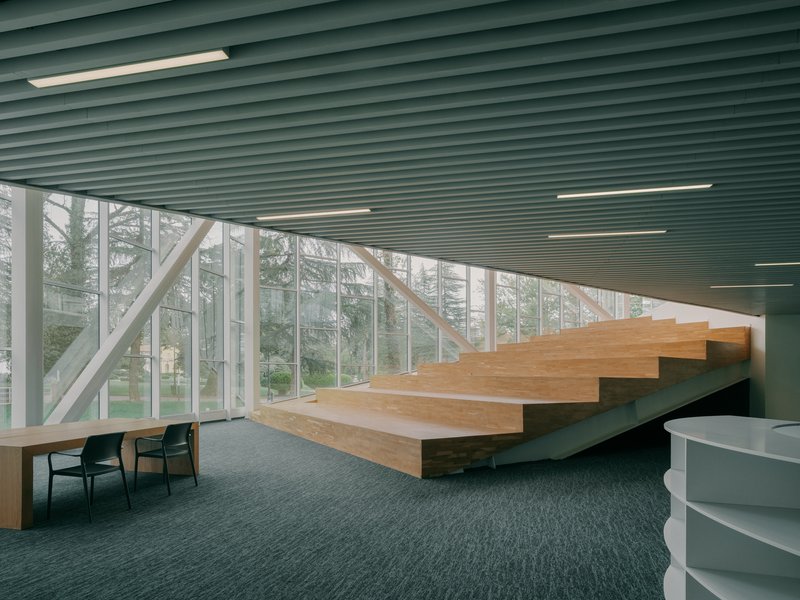 Floating timber staircase beneath a green ribbed ceiling with floor-to-ceiling glazing overlooking a park