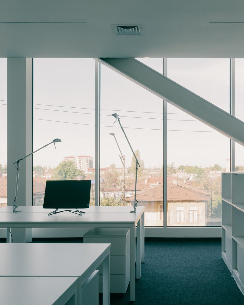 Workstation with task lamps facing floor-to-ceiling windows overlooking suburban rooftops on an overcast day