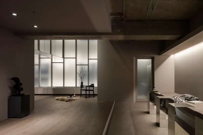 Interior gallery space with backlit translucent glass panels and exposed concrete beam ceiling