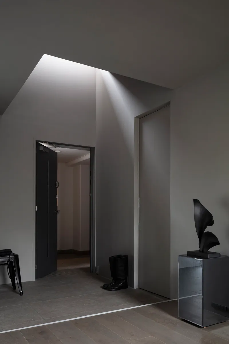 Angled skylight above doorway casting diagonal shadow down pale grey walls and polished floor