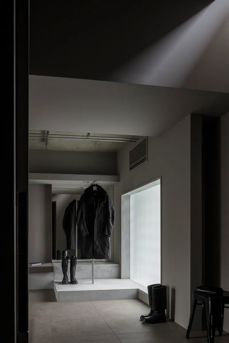 Entry hall with concrete platform displaying coat and boots beneath translucent glass panel