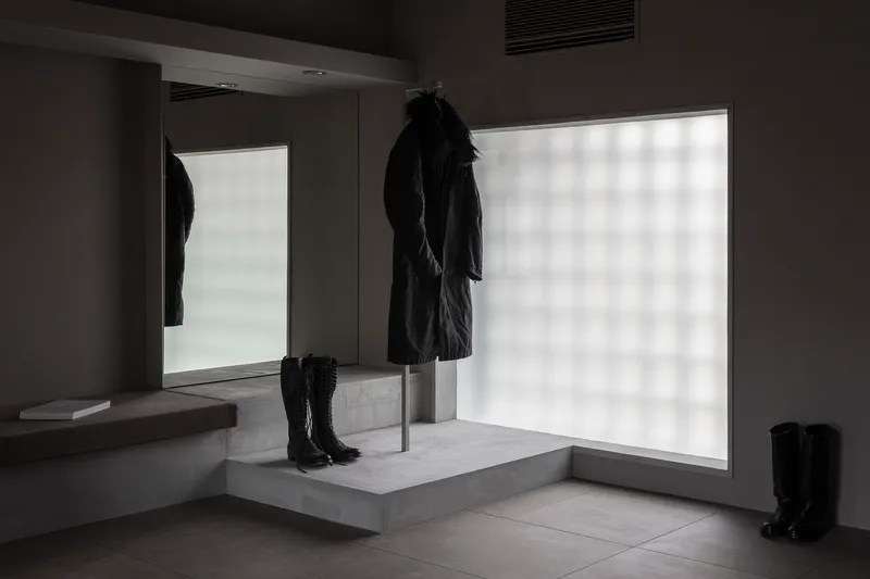 Concrete display pedestal with coat on steel rod and boots against backlit frosted glass