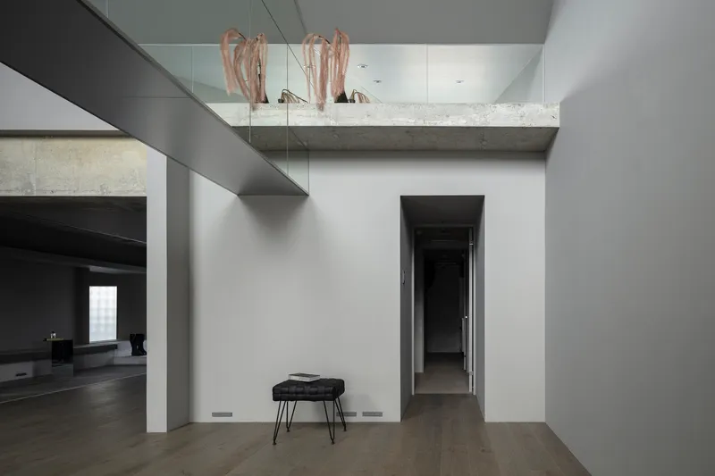 Double-height space with exposed concrete beam and mezzanine level above painted corridor