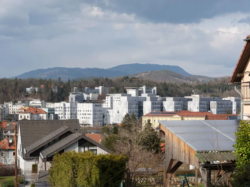White cubic volumes rising above existing rooftops with mountains in the distance under cloudy skies