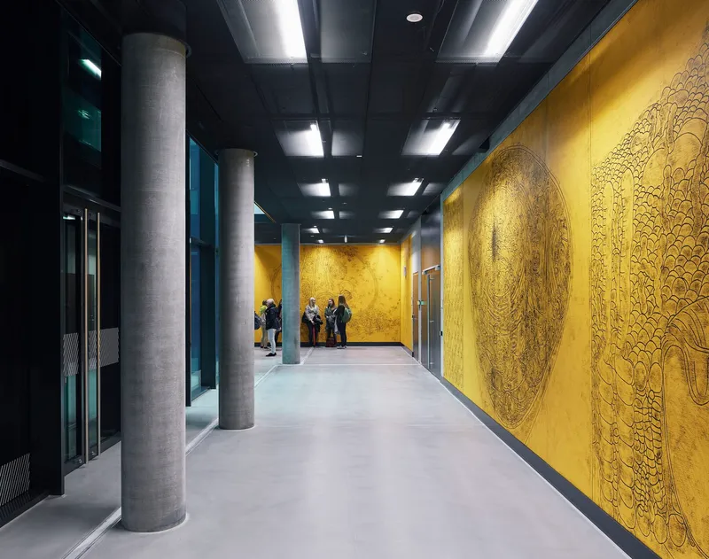 Elevator lobby with circular concrete columns and embossed gold wall panels beside the lift doors