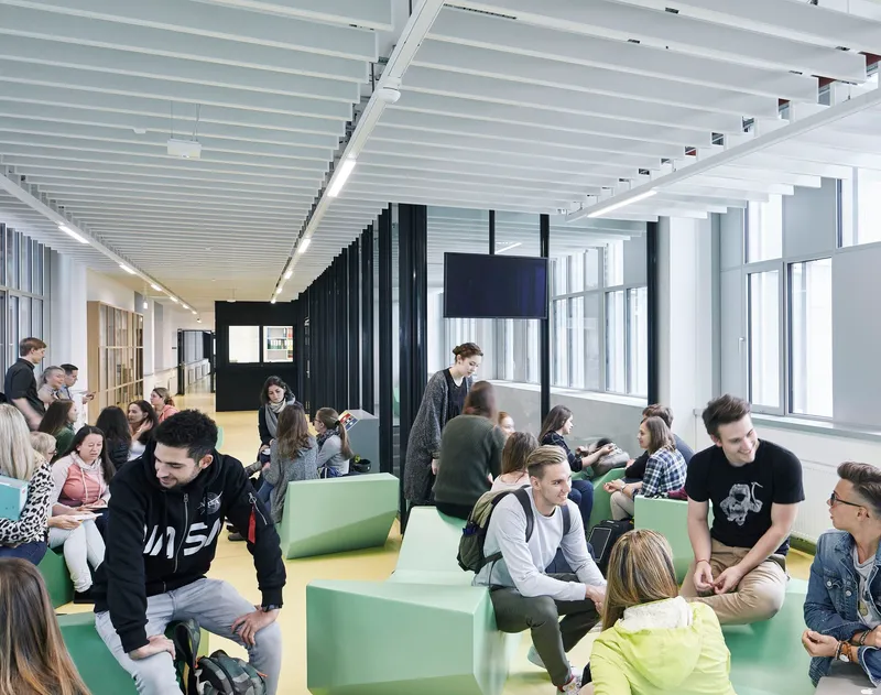 Open lounge space with lime green modular seating and students gathering beneath linear ceiling panels