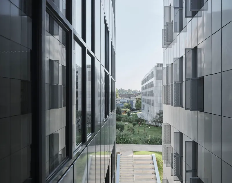 View between two aluminum-clad building volumes framing a landscaped courtyard with central stone steps