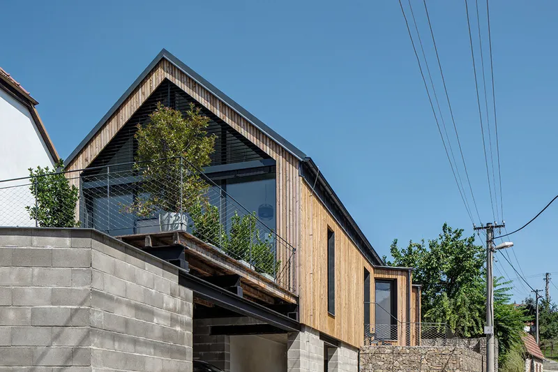 Vertical timber cladding and concrete block base with gabled roof terrace under clear blue sky