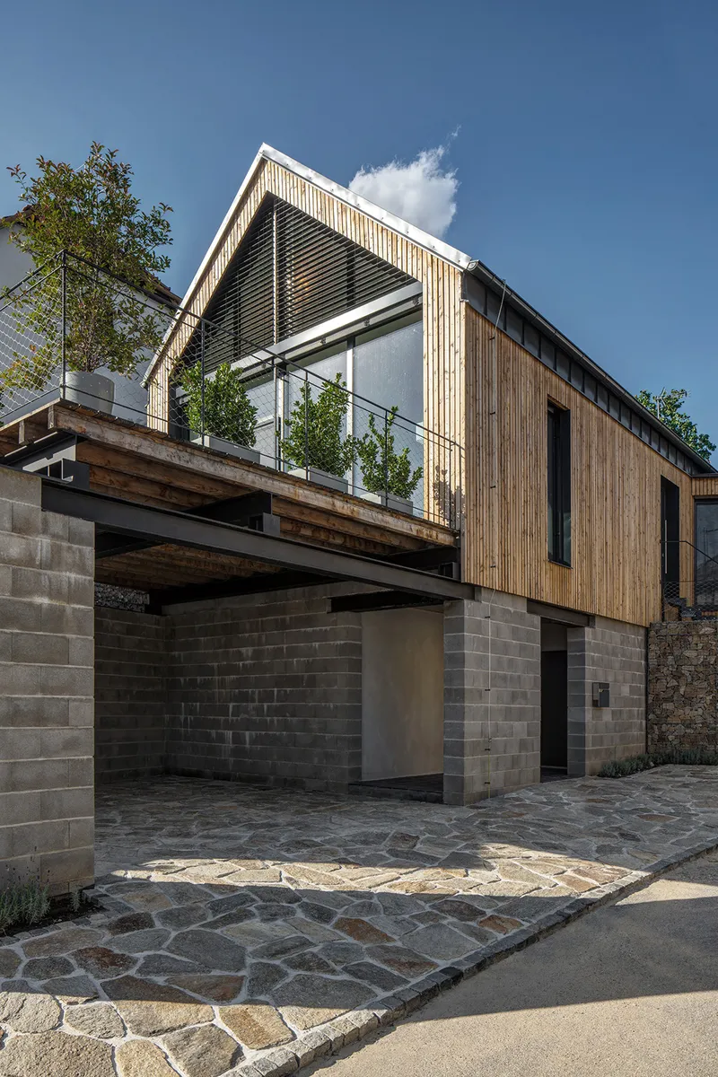 Stone paved entrance courtyard beneath cantilevered timber beams and upper level balcony with plantings