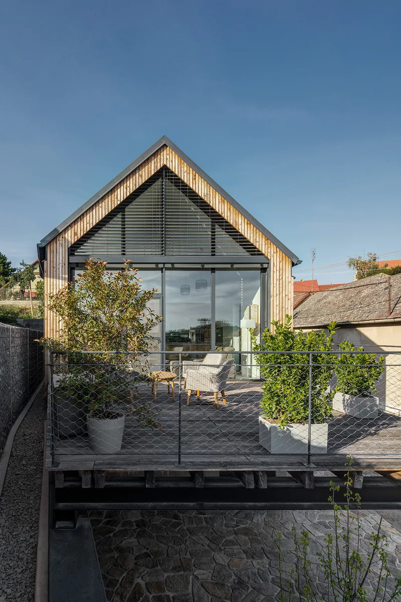 Rooftop terrace with chain-link fencing and potted trees facing glass gable facade