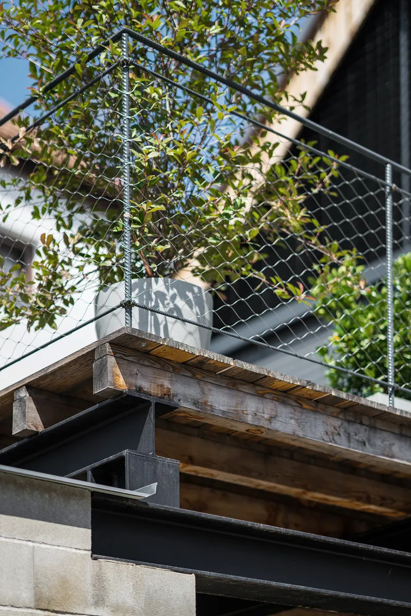 Detail of reclaimed timber beam supporting metal deck with climbing vines on chain-link railing