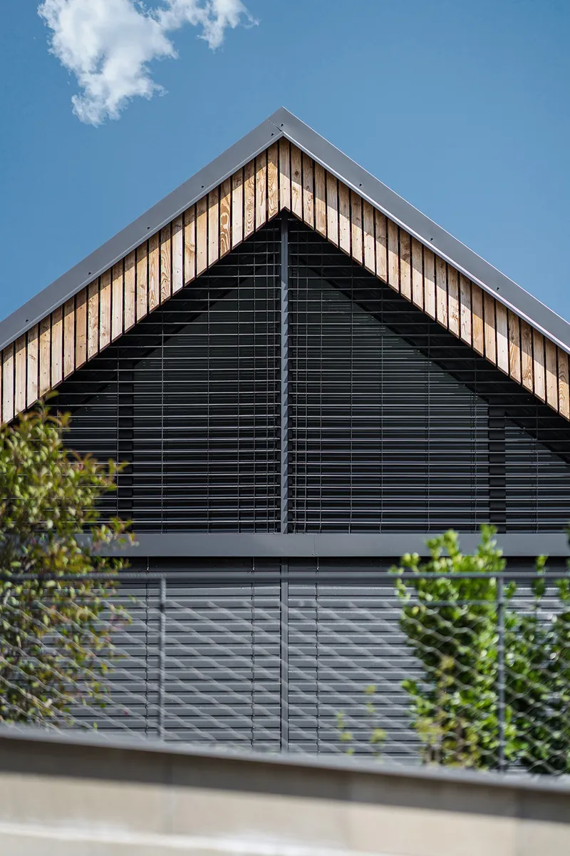 Gable end with horizontal timber slats and black louvered screens framed by foliage