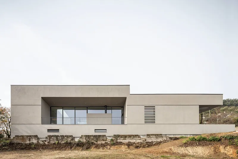 Minimalist façade with clean horizontal geometry embedded in a sloped terrain.