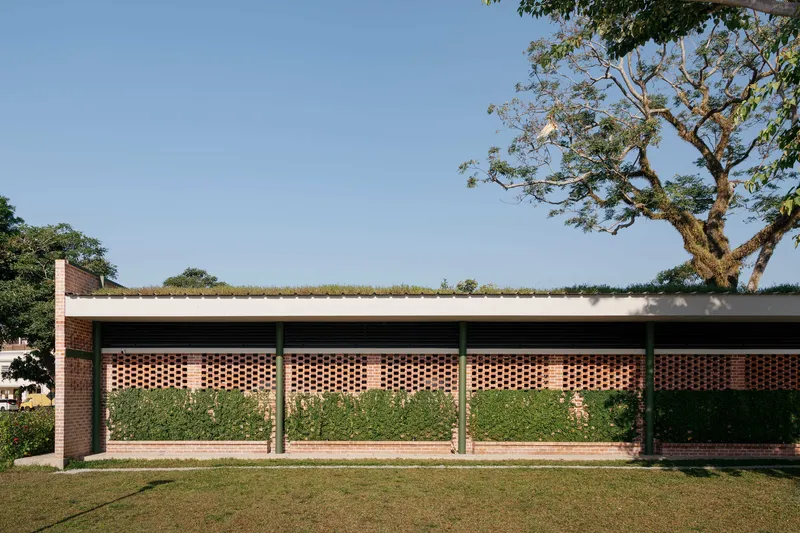 Perforated brick facade panels separated by columns beneath a planted roof and overhanging tree branch