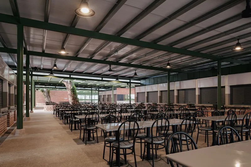 Dining hall interior with rows of tables and chairs under exposed green steel beams and pendant lighting
