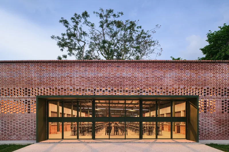 Brick facade with perforated band above fully glazed entrance doors revealing the lit interior at dusk