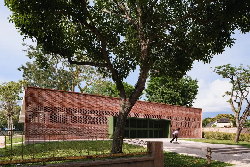 Perforated brick facade with recessed entrance framed by mature trees and lawn