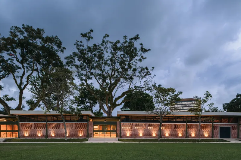 Perforated brick facade with uplighting at dusk beneath a timber and steel canopy overhang