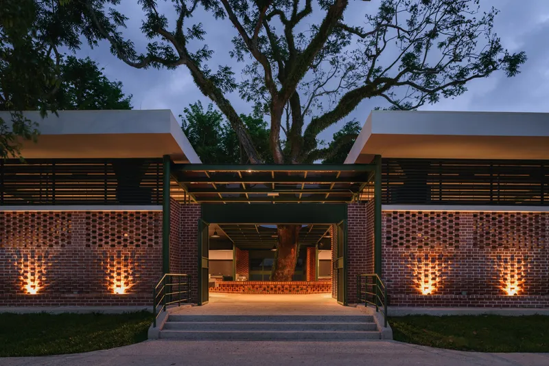 Covered entry portico with timber pergola framing the illuminated brick walls and glass doors at twilight