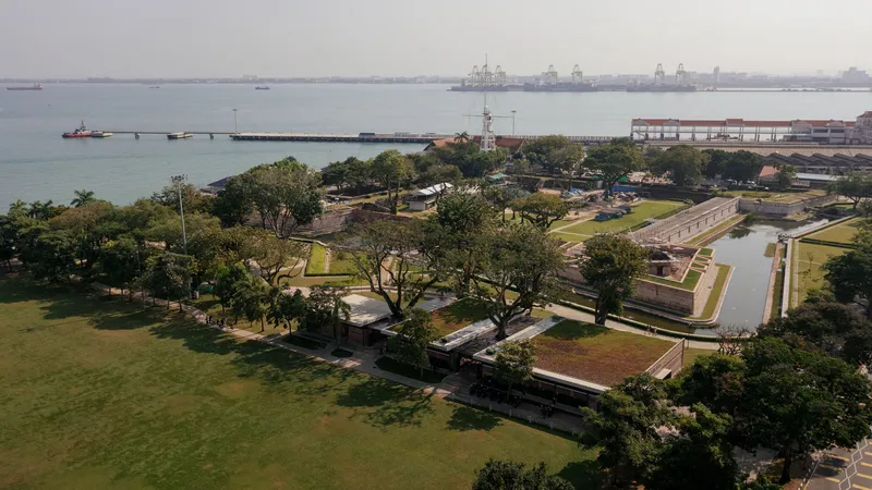 Aerial view of the pavilion complex with waterfront, harbor cranes, and park lawns in late afternoon light