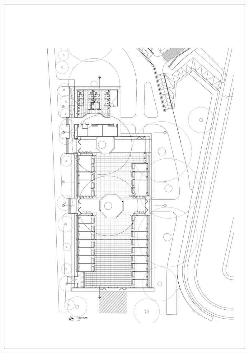 Site plan drawing showing three rectangular volumes with central courtyard and surrounding pathways and trees