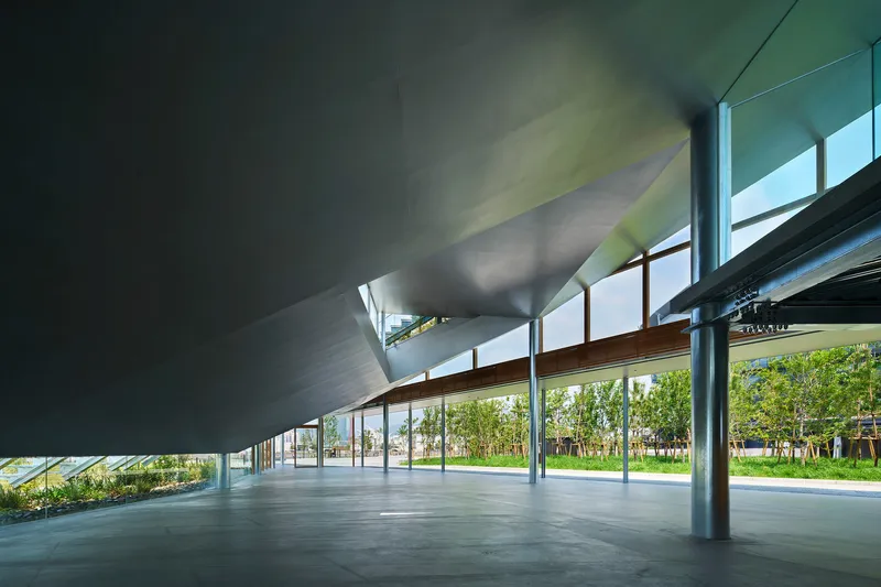 Interior space beneath the sloping roof with steel columns and glazed walls overlooking planted landscape