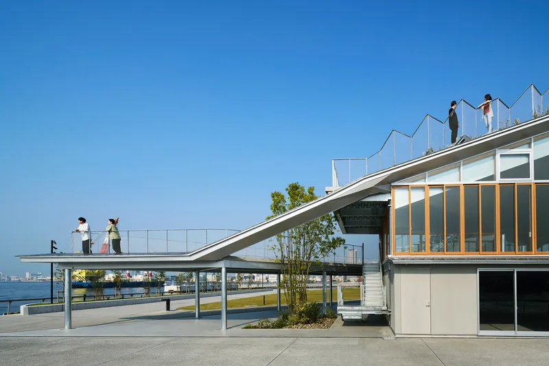 Diagonal roof plane with people standing above glazed facade and waterfront view beyond