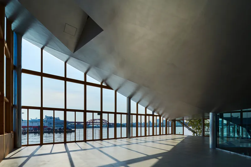 Sunlit corridor with timber curtain wall overlooking water and angled concrete ceiling plane above